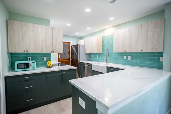 Retro Kitchen Remodel - This kitchen remodel was a complete transformation that created a spacious, modern, and functional living area, designed to meet the client's unique style and preferences.
Opened the Space: We took down a dividing wall between the kitchen and the dining room, instantly creating an open-concept layout that enhances the flow between the spaces and invites more natural light.

New Flooring Throughout: 
All the flooring in the home was replaced, providing a consistent and cohesive look from the kitchen into the rest of the house. The new flooring adds a fresh, contemporary feel that complements the kitchen's modern design.

Popcorn Ceiling Removal: 
The dated popcorn ceilings were removed throughout the entire home, offering a cleaner, more modern aesthetic and improving the overall appearance of each room.
Two-Tone Cabinets: We installed new, two-tone cabinetry as requested by the client. The combination of light wood upper cabinets and deep-toned lower cabinets adds visual interest and a stylish contrast to the kitchen's design.

Blue Subway Tile Backsplash: 
A striking blue subway tile backsplash was installed, bringing a pop of color to the space and tying together the modern aesthetic with a playful yet sophisticated touch.

Farmhouse Sink: 
A farmhouse-style sink was added, combining modern convenience with a timeless, rustic appeal. This sink enhances both the functionality and the charm of the kitchen.

Fresh Paint Throughout: 
The entire home was repainted, including the kitchen, to create a fresh, cohesive look that ties together all of the renovated spaces.

Recessed Lighting: 
New recessed lighting was installed throughout the kitchen, providing ample illumination and a sleek, modern look. These lights brighten up the space and highlight the clean lines and modern design elements.

Electrical Upgrades: 
The electrical system was updated to support the new lighting fixtures and other modern elements in the kitchen. This ensures the home is up-to-date with current electrical standards while enhancing its overall design.

This remodel completely transformed the kitchen and surrounding areas, creating an open, inviting, and stylish space that suits the client’s vision and enhances the overall functionality of the home.