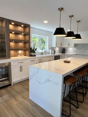 Kitchen Remodel - Pinecrest - Our selection of custom kitchen cabinets allow you to personalize every detail, from cabinet color to door style. This custom transitional kitchen seamlessly blends shaker and slab door styles, embracing both modern and traditional elements, as the wood-toned display area serves as the focal point. The white quartz countertops, featuring a waterfall kitchen island, create a bright atmosphere. Enjoy our complimentary kitchen design services to bring your dream custom kitchen cabinet layout to life.