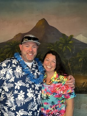 Photo Booth at the Royal Islanders in Mesa, Az - Guests pose against a tropical backdrop at Royal Islanders in Mesa, Arizona featuring lush palm leaves, tiki torches, and colorful hibiscus flowers. The photo booth props like flower leis add a playful touch.