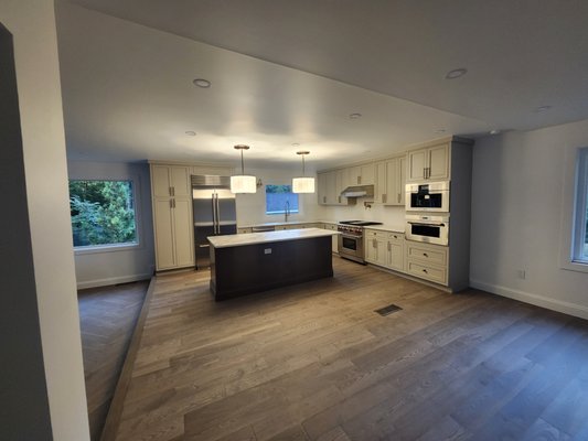 Franklin Park Home Renovation - This dated, windowless galley kitchen—once cramped and dimly lit—has been transformed into a bright, open-plan culinary hub. By removing walls and reconfiguring the layout, the space now flows seamlessly into the adjacent living area. Custom oak cabinetry maximizes storage while maintaining clean lines, paired with premium stainless steel appliances and a large center island for prep and casual dining. New large windows flood the room with natural light, highlighting quartz countertops and a handcrafted tile backsplash. The living room features a custom built-in media unit with integrated storage and display shelving, new recessed LED lighting throughout for layered ambiance, and new engineered hardwood flooring—finished with a striking herringbone pattern in the living room that adds timeless elegance and warmth to the entire open space.