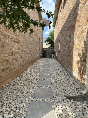 Rock Garden With Stepping Stones - River rock is a sleek and simple solution to avoid the tedious labor of weeding walkways. All while improving drainage, river rock helps prevent erosion and offers a natural, polished look to your outdoor spaces. When paired with paver stepping stones, it creates a durable, low-maintenance pathway that is easy to navigate. The combination provides both functionality and aesthetic appeal, ensuring a clean, elegant solution for high-traffic areas and enhancing the overall design of your landscape. Additionally, the contrast between the smooth river rocks and the sturdy pavers adds visual interest and complements various architectural styles. Rock Garden With Stepping Stones - River rock is a sleek and simple solution to avoid the tedious labor of weeding walkways. All while improving drainage, river rock helps prevent erosion and offers a natural, polished look to your outdoor spaces. When paired with paver stepping stones, it creates a durable, low-maintenance pathway that is easy to navigate. The combination provides both functionality and aesthetic appeal, ensuring a clean, elegant solution for high-traffic areas and enhancing the overall design of your landscape. Additionally, the contrast between the smooth river rocks and the sturdy pavers adds visual interest and complements various architectural styles.