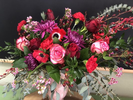 Exploding with Passion! - Exploding with Passion - Half a Dozen Roses, Anemones, Mums and Fragrant Seasonal Blooms with an Array of Premium Greens.
Boom, baby! A passionate and vibrant array of Premium Roses, Seasonal Anemones, Chrysanthemums, Dianthus, Fragrant Wax Flower and Premium Mixed Eucalyptus! Designed in a deco pedestal stone vase with love! Sure to fill any room with an electric energy and an incredible fragrance.