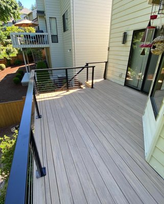 Trex Composite deck with metal railing - This modern deck design features a composite decking surface, offering low maintenance and durability, perfect for year-round use. The sleek black metal railing with cable infill enhances the deck's contemporary look, providing an unobstructed view of the surrounding landscape. The clean lines and neutral tones make this deck a stylish and functional extension of the home. Trex Composite deck with metal railing - This modern deck design features a composite decking surface, offering low maintenance and durability, perfect for year-round use. The sleek black metal railing with cable infill enhances the deck's contemporary look, providing an unobstructed view of the surrounding landscape. The clean lines and neutral tones make this deck a stylish and functional extension of the home.