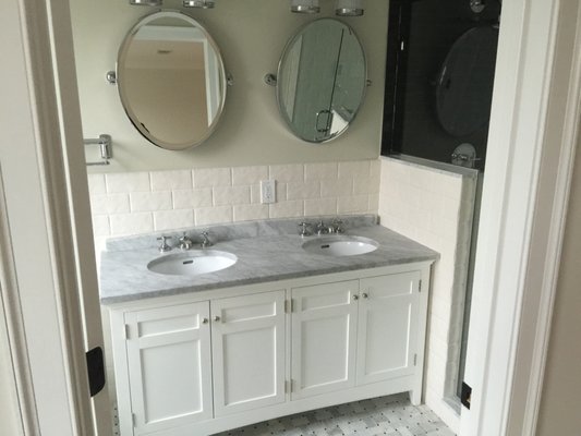 Timeless Marble Bathroom Renovation - This timeless bathroom renovation features elegant finishes and thoughtful details throughout. We installed custom white vanities with soft-close cabinetry and polished marble countertops for a clean, classic aesthetic. The floors are finished in a basketweave marble mosaic, offering both texture and visual interest while tying in seamlessly with the polished chrome fixtures.
In the primary bath, we added double sinks, round framed mirrors, and soft wall lighting to create a cozy, refined atmosphere. The shower features hand-laid tile in contrasting tones, with a glass enclosure and upgraded plumbing fixtures for a sleek finish. Light cream wall tile and smooth transitions between materials give the space a warm, welcoming feel.
From vintage-inspired textures to modern functionality, this renovation balances comfort and craftsmanship in every detail.