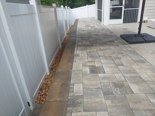 Chappel patio - We installed a retaining wall 80 ft long and about 2 feet high at lowest point . Then we installed around 340 sq ft of patio that would tie into the retaining wall. We had to cap off existing irrigation lines and we changed downspouts from black corrugated pipe to white pvc and extended them to beyond the wall/patio area .
We installed a step and landing at the front gate and a landing at the back gate. We installed black fabric and river rock around the entire perimeter of patio to match the front but also to help with drainage. This job took about a month to complete from start to finish with the enhancements in both front and back. Chappel patio - We installed a retaining wall 80 ft long and about 2 feet high at lowest point . Then we installed around 340 sq ft of patio that would tie into the retaining wall. We had to cap off existing irrigation lines and we changed downspouts from black corrugated pipe to white pvc and extended them to beyond the wall/patio area .
We installed a step and landing at the front gate and a landing at the back gate. We installed black fabric and river rock around the entire perimeter of patio to match the front but also to help with drainage. This job took about a month to complete from start to finish with the enhancements in both front and back.