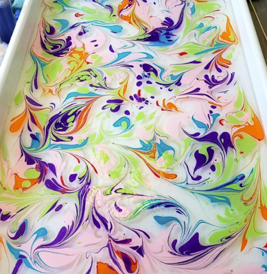 Water Marbling - Water marbling is an ancient artform that originated in the fifteenth century. Ebru (Turkey) and Suminagashi (Japan) are still in use today.
The technique consists of dropping pigments (most commonly acrylics) onto an aqueous solution. The floating pigments can then be moved around with different tools to create unique patterns and designs. Your final design is then permanently transferred onto a treated silk scarf. This activity is great for all ages! Water Marbling - Water marbling is an ancient artform that originated in the fifteenth century. Ebru (Turkey) and Suminagashi (Japan) are still in use today.
The technique consists of dropping pigments (most commonly acrylics) onto an aqueous solution. The floating pigments can then be moved around with different tools to create unique patterns and designs. Your final design is then permanently transferred onto a treated silk scarf. This activity is great for all ages!