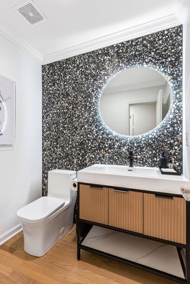 Powder Room - This powder room packs a visual punch with its modern design, elevated material choices, and gallery-like execution — proof that small spaces can still make big impressions.
Highlights of the transformation include:
Terrazzo-Inspired Feature Wall: The stunning black tile wall, speckled with warm and cool tones, brings texture and energy to the space — creating a high-design backdrop that anchors the room.
Backlit Circular Mirror: A floating, halo-lit mirror adds soft, ambient lighting while doubling as a sculptural element.
Modern Floating Vanity: Ribbed wood cabinetry with sleek black pulls delivers warmth and dimension, while the integrated sink keeps the lines clean and contemporary.
Luxury Touches: Matte black accessories, custom tray styling, and curated decor give this powder room a hotel-lobby vibe.
With every detail considered — from the lighting to the tile to the wood grain — this remodel transformed a basic half bath into a memorable moment. It’s not just a powder room, it’s a conversation starter. Powder Room - This powder room packs a visual punch with its modern design, elevated material choices, and gallery-like execution — proof that small spaces can still make big impressions.
Highlights of the transformation include:
Terrazzo-Inspired Feature Wall: The stunning black tile wall, speckled with warm and cool tones, brings texture and energy to the space — creating a high-design backdrop that anchors the room.
Backlit Circular Mirror: A floating, halo-lit mirror adds soft, ambient lighting while doubling as a sculptural element.
Modern Floating Vanity: Ribbed wood cabinetry with sleek black pulls delivers warmth and dimension, while the integrated sink keeps the lines clean and contemporary.
Luxury Touches: Matte black accessories, custom tray styling, and curated decor give this powder room a hotel-lobby vibe.
With every detail considered — from the lighting to the tile to the wood grain — this remodel transformed a basic half bath into a memorable moment. It’s not just a powder room, it’s a conversation starter.