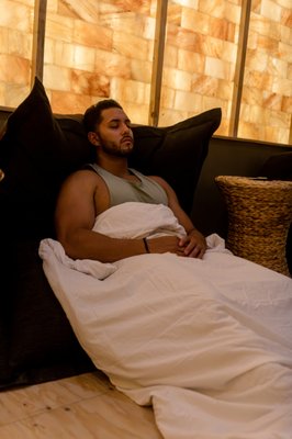 Salt Therapy Lounge - Experience deep relaxation in our serene, shared Salt Therapy Lounge. Therapeutic salt is gently infused into the air for a treatment known as Halotherapy, or simply Salt Therapy—a natural way to support respiratory health, skin wellness, and stress relief.

Settle into an oversized beanbag surrounded by softly glowing Himalayan salt brick walls, complete with a weighted blanket and heated eye mask for ultimate comfort and calm.

After your session, enjoy two full hours of access to our wellness bathhouse — including soaking pools, sauna, steam room, cold plunge and lounge spaces. It’s the perfect way to unwind, detox, and restore balance.