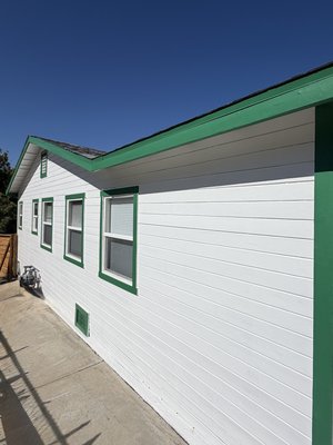 High-Contrast Ranch Revive - This exterior transformation highlights the home's modern ranch-style aesthetic with a clean white body accented by a crisp, two-tone green palette. Sharp, meticulous cut-ins wrap the deep forest green trim around the windows, fascia, and porch railings, while the large supporting columns are finished in a smooth, elegant sage green finish. The clean craftsmanship extends all the way to the street side, where a solid, ultra-crisp coat of white paint on the masonry retaining wall creates a striking, high-contrast foundation that makes the rich, golden-brown tones of the horizontal wood privacy fence truly pop. High-Contrast Ranch Revive - This exterior transformation highlights the home's modern ranch-style aesthetic with a clean white body accented by a crisp, two-tone green palette. Sharp, meticulous cut-ins wrap the deep forest green trim around the windows, fascia, and porch railings, while the large supporting columns are finished in a smooth, elegant sage green finish. The clean craftsmanship extends all the way to the street side, where a solid, ultra-crisp coat of white paint on the masonry retaining wall creates a striking, high-contrast foundation that makes the rich, golden-brown tones of the horizontal wood privacy fence truly pop.