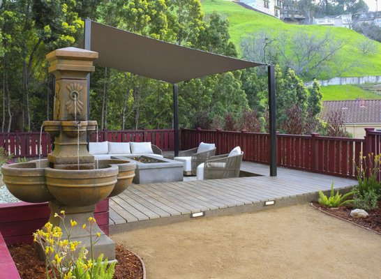 Hillside Backyard Paradise - At this home we installed a Custom Concrete gas fire pit with volcanic rock and a wide top for drinks, plates, etc. For lighting, we installed Bollard style low-voltage LED lights, along with Surf Green 3/4" crushed gravel with weed fabric. For plants, we used New Zealand Flax, Kangaroo Paw, Lavender, Salvia, with drip irrigation and boulders. Surrounding the fire pit we created a solid stained "Cabernet" Redwood railing, encircled by stabilized Decomposed Granite. The fountain you see is from Reseda Discount Pottery, and the deck was made from Trex Transcend "Spiced Rum" with a pressure-treated wood frame and step lights. For shade we installed a rectangular shade sail from Sunbrella with heavy-duty posts, bollard lights, and prefab furniture.
Needless to say our customer was overjoyed with the result and has a paradise in their own backyard.