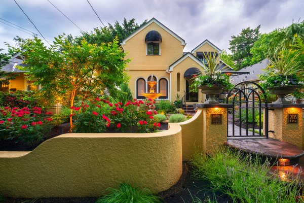 Mediterranean Flair - This front yard consisted of a boring lawn flanked with a boxwood hedge that ran alongside a bland and narrow concrete driveway and walkway. There was nothing to tie the generic landscape to the lovely Mediterranean inspired house. All that changed with the design and installation done by Blessing Landscapes.
A stucco retaining wall with sensuous curves and rounded steps leads to a gate inspired by the lead glass windows. The stamped concrete path widens to the expanded driveway and also continues to another set of rounded steps to the recessed front door. Centered on the left side windows, an elegant fountain bubbles away. A narrow-decomposed granite pathway with architectural pavers circles the fountain and is flanked by Lavender and Santolina. Two Crape Myrtles give the garden a bit of symmetry and along with several beautiful containers add a sense of elegance and drama to the garden. The clients love of roses is apparent from the quantity and variety that are tucked into every bed. The rich textures and colors from the roses and other plantings such as Pittosoporum, Nepeta and New Zealand Flax are highlighted by accent lighting which makes the whole garden come alive at night. Mediterranean Flair - This front yard consisted of a boring lawn flanked with a boxwood hedge that ran alongside a bland and narrow concrete driveway and walkway. There was nothing to tie the generic landscape to the lovely Mediterranean inspired house. All that changed with the design and installation done by Blessing Landscapes.
A stucco retaining wall with sensuous curves and rounded steps leads to a gate inspired by the lead glass windows. The stamped concrete path widens to the expanded driveway and also continues to another set of rounded steps to the recessed front door. Centered on the left side windows, an elegant fountain bubbles away. A narrow-decomposed granite pathway with architectural pavers circles the fountain and is flanked by Lavender and Santolina. Two Crape Myrtles give the garden a bit of symmetry and along with several beautiful containers add a sense of elegance and drama to the garden. The clients love of roses is apparent from the quantity and variety that are tucked into every bed. The rich textures and colors from the roses and other plantings such as Pittosoporum, Nepeta and New Zealand Flax are highlighted by accent lighting which makes the whole garden come alive at night.