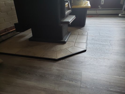3 different floor heights brought to One level floating vinyl floor - This home had varying subfloor heights with ceramic tile in the entry way, linoleum in the kitchen and carpet in the living room and bar area. We removed the different flooring, leveled the subfloor to almost perfect (this job did not allow for perfect without a hefty price tag) and installed a floating vinyl floor throughout, complete with a new stone hearth to replace the cinder blocks and cracked ceramic