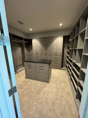 Sophisticated Main Closet - We turned this entire room into a closet providing a dark wood grain finish with plenty of drawer space. The center island has a black Thinscape countertop with tilt out hampers below to store any laundry accessibly and out of sight. This closet has everything from lots of hanging and shelving, to doors and drawers, giving it a sophisticated and pleasant feel and design.