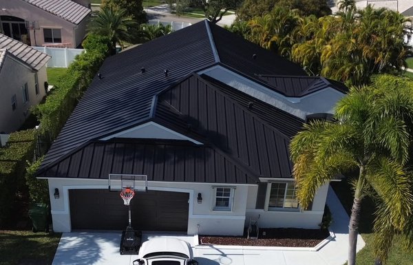 Eloquent - This striking new roof showcases the timeless elegance and durability of standing seam metal roofing. The sleek, matte-black finish complements the clean lines of the home’s modern architecture, creating a bold contrast against the light exterior walls.

Each seam runs vertically, uninterrupted from eave to ridge, lending a sense of height and sophistication while ensuring superior protection against the elements. The precision of the panel alignment and the crisp edges speak to expert craftsmanship, elevating the curb appeal of the entire property.