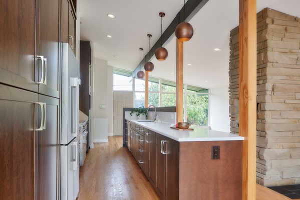 Cherry Wood Kitchen Remodel - This kitchen’s transformation took it from a cramped and compartmentalized trio of spaces to a streamlined, open-concept showpiece. By removing awkward partial walls and rethinking the galley layout, the design team created a more inviting flow that ties together the kitchen, dining, and living areas. Custom cherry shiplap half walls maintain a sense of definition without blocking the view, while a new bar seating area offers a perfect perch overlooking the lush backyard. Ample quartz counter space, newly installed tall cabinetry, and open shelving add both practicality and personality, all coming together to bring fresh life and energy into this once-constrained space.