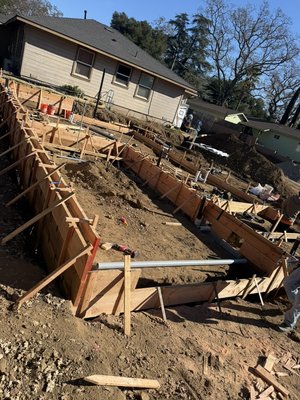 4 home development in Atascadero Ca - Photo 1 – Foundation Formwork & Underground Rough-In
This photo shows the foundation phase under construction, with continuous concrete footing forms fully installed and braced. Wood formwork outlines the structural footprint, including interior and perimeter footings. Underground plumbing stub-outs and sleeves are in place and properly positioned prior to concrete placement. Soil conditions have been excavated to required depths, with clean, straight forms indicating preparation for inspection and upcoming concrete pour.

Photo 2 – Site Preparation & Pad Grading
This photo captures the site preparation and grading stage prior to foundation work. The building pad has been rough-graded and compacted, with layout stakes clearly marking elevations, setbacks, and reference points. Temporary erosion control measures are visible along the perimeter. The area is cleared and prepared for formwork, reinforcing steel installation, and subsequent concrete operations.