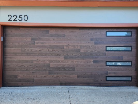 Custom Garage Door Sedona - Enhance your property’s style with this custom garage door in a distinctive Kona Plank finish. Designed with insulated windows for natural light and comfort, this door also features a beautiful wood grain finish for added curb appeal. Our team handled expert installation, and all hardware is powder coated for lasting durability and a sleek look. Custom Garage Door Sedona - Enhance your property’s style with this custom garage door in a distinctive Kona Plank finish. Designed with insulated windows for natural light and comfort, this door also features a beautiful wood grain finish for added curb appeal. Our team handled expert installation, and all hardware is powder coated for lasting durability and a sleek look.