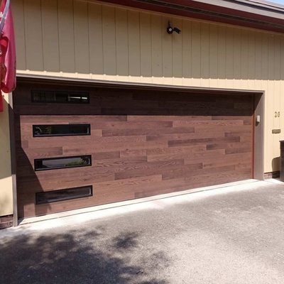 Plank Style Garage Door - This is a Clopay Modern Steel with the customer "Kona" wood finish, with contemporary black framed slim windows down the left side. The size of the door will vary the price. This price is based on a 16x7 two car garage. Plank Style Garage Door - This is a Clopay Modern Steel with the customer "Kona" wood finish, with contemporary black framed slim windows down the left side. The size of the door will vary the price. This price is based on a 16x7 two car garage.