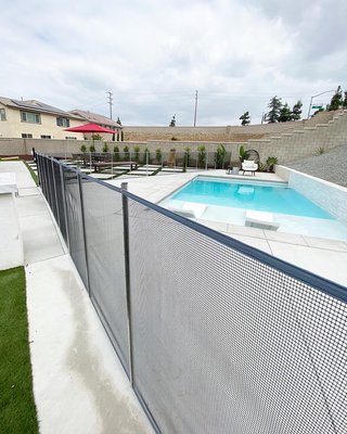 Modern backyard newly remodeled with pool. Gray border with black clearview mesh fence installed for safety. - This newly remodeled backyard looks perfect with the black clear view mesh and gray border pool fence by Lakeview Pool Fencing! Keep your children & pets safe this summer!