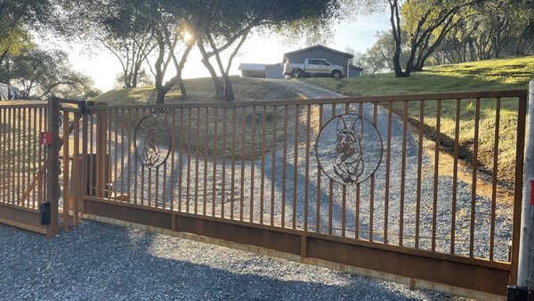 Cool Cantilevered Gate - This is a unique gate that was built robust and to the customer's liking. Its a cantilevered gate, sliding on Italian rollers without a track. The customer wanted the gate to match the rustic feel the Town of Cool has, so they requested the gate to be "rusted" or "weathered" instead of painted. We built a custom man gate, with keypad entry, next to the entrance gate for easy access in and out of their property. As you can tell, their dogs are their world so we added plasma cutouts on the gate, as well as dog paw prints through out. They love how smooth their gate operates without a track on the ground. Cool Cantilevered Gate - This is a unique gate that was built robust and to the customer's liking. Its a cantilevered gate, sliding on Italian rollers without a track. The customer wanted the gate to match the rustic feel the Town of Cool has, so they requested the gate to be "rusted" or "weathered" instead of painted. We built a custom man gate, with keypad entry, next to the entrance gate for easy access in and out of their property. As you can tell, their dogs are their world so we added plasma cutouts on the gate, as well as dog paw prints through out. They love how smooth their gate operates without a track on the ground.