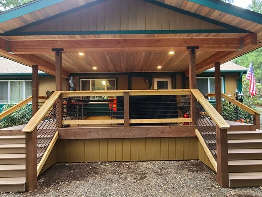 Covered Deck - Welcome to the pinnacle of outdoor living – our breathtaking covered deck, where craftsmanship meets natural beauty in perfect harmony. Crafted with care and attention to detail, this haven is a celebration of the great outdoors, offering both shelter and serenity in equal measure.

Step onto the luxurious composite decking, renowned for its durability and stunning aesthetics, sets the stage for countless moments of relaxation and connection with nature.

But the allure doesn't end there – gaze upward to behold the captivating sight of a blue pine ceiling, a symphony of rich hues and intricate grains that infuse the space with warmth and character. Every glance upwards is a reminder of the majesty of the natural world, inviting you to pause and appreciate the beauty that surrounds you.

As you lean against the sturdy rebar railing, feel the cool metal beneath your fingertips and marvel at its understated elegance. Designed to blend seamlessly with the surroundings while offering unparalleled safety and support, this railing is both functional and fashionable, a testament to the artistry of our craftsmen.

Whether you're hosting a summer barbecue, sipping morning coffee, or simply basking in the beauty of a starlit evening, our composite deck promises to be a sanctuary of relaxation and rejuvenation. So contact us today so we can make your vision of the perfect outdoor space a reality!