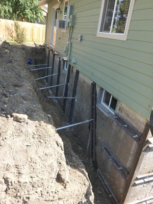 Foundation repair, leaning and broken wall - This foundation wall was 8' out of plumb, the wall had also broken at the mid-point, with the portion of the wall above the fracture translating inward by 2-3". There was also significant water intrusion into the basement. We installed lateral helical piers to correct and support the leaning wall. We used the vertical c-channel sections, through bolted into a matching channel on the interior surface of the wall to correct the horizontal fracture/translation. The entire exterior of the home was encapsulated in a drain panel to mitigate any future water infiltration issues. Foundation repair, leaning and broken wall - This foundation wall was 8' out of plumb, the wall had also broken at the mid-point, with the portion of the wall above the fracture translating inward by 2-3". There was also significant water intrusion into the basement. We installed lateral helical piers to correct and support the leaning wall. We used the vertical c-channel sections, through bolted into a matching channel on the interior surface of the wall to correct the horizontal fracture/translation. The entire exterior of the home was encapsulated in a drain panel to mitigate any future water infiltration issues.