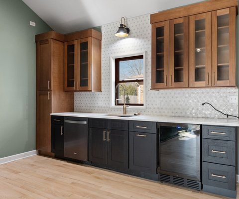 Warm Modern Two-Tone Kitchen Remodel – Libertyville - Check out this custom kitchen transformation by 4Ever Remodeling in Libertyville! We brought contrast and character into the space using a two-tone cabinetry layout, mixing warm wood uppers with sleek black base cabinets by Forevermark. Bright Da Vinci Gold quartz counters and an MSI Citadel Gold Trident geometric mosaic backsplash brighten up the room while adding a touch of gold detailing. Finished with under-cabinet lighting, a built-in drink fridge, and fresh hardwood floors. Looking to upgrade your kitchen? Contact 4Ever Remodeling today for a design consultation! Warm Modern Two-Tone Kitchen Remodel – Libertyville - Check out this custom kitchen transformation by 4Ever Remodeling in Libertyville! We brought contrast and character into the space using a two-tone cabinetry layout, mixing warm wood uppers with sleek black base cabinets by Forevermark. Bright Da Vinci Gold quartz counters and an MSI Citadel Gold Trident geometric mosaic backsplash brighten up the room while adding a touch of gold detailing. Finished with under-cabinet lighting, a built-in drink fridge, and fresh hardwood floors. Looking to upgrade your kitchen? Contact 4Ever Remodeling today for a design consultation!