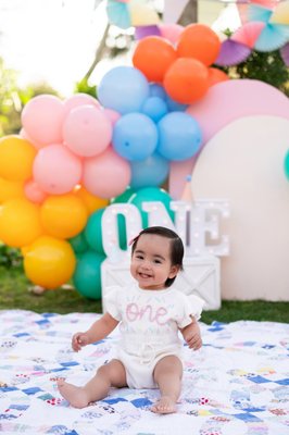 Cake Smash Portraits - There’s nothing quite like my cake smash sessions! It’s a perfect way to celebrate your little one’s first milestone. From the vibrant decorations to the messy, frosting-covered smiles, these sessions are filled with unforgettable moments.
Claire’s cake smash starts with a fun and colorful setup! Whether you opt for pastel hues, bold brights, or a theme inspired by your little one’s favorite characters, the backdrop sets the stage for adorable memories. Balloons, banners, and a beautifully decorated cake bring everything together.
The cake is the star of the show (aside from your little one, of course)! A small, soft cake with fluffy frosting is best for easy smashing and messy fun. We chose colors that pop and coordinate with the theme. Your little one will enjoy filling their hands with frosting and trying to get their fingers into their mouth. 
Your set will be ready when you arrive, once Claire was changed it was time for the fun to begin! We took portraits, and changed for the cake smash portion of the session. Some little ones dive right in, while others need a bit of encouragement. A few tips to make the session a success:
Let your baby explore the cake at their own pace.
Play some favorite songs to keep them comfortable.
Have a few small toys or snacks handy for extra engagement.
I’m always ready, the best shots come when you least expect them!
As a photographer, my goal is to capture every giggle, curious glance, and frosting-covered finger. Close-up shots of tiny hands digging into the cake, wide shots of the entire scene, and candid moments of pure delight create a full story of this special milestone.
A first birthday cake smash is more than just a photoshoot—it’s a celebration of your baby’s first big year AND you making it one year as a parent! If you’re ready to create lasting memories with a fun and unique session, let’s chat! Contact me today to book your little one’s cake smash experience.
Let’s make some sweet memories together!