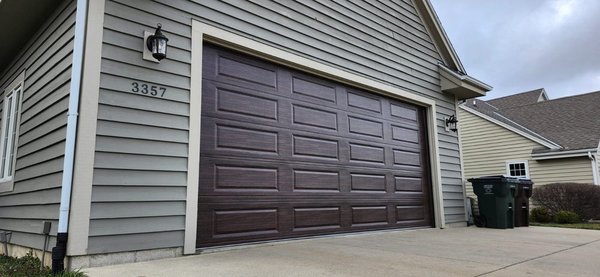 Warm Refresh: Raised Long Panel in Modern Woodgrain - We replaced a slightly damaged white sectional door with a Raised Long Panel design in a rich Modern Woodgrain color. The new door adds warmth, depth, and a polished finish that elevates the entire exterior.