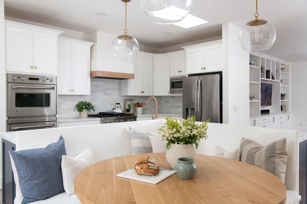 Modern Coastal Kitchen Remodel in Newport Beach - This stylish Newport Beach kitchen remodel includes calming shades of blue, warm wood elements, abundant natural light, and an airy, uncluttered feel.

Touches of warm toned honey bronze cabinet pulls and knobs look stunning on resurfaced white cabinets. The kitchen faucet and soap dispenser in luxe gold brings an elegant flair to the single bowl apron sink sitting atop a navy blue L shaped island. A custom exhaust hood with a white oak natural trim reinforces the connection between the indoors and out. Finishing touches of aged brass and clear glass light fixtures creates a soothing and timeless effect.

Opposite the kitchen lies an accent wall in silver Pincord wallpaper, white shaker cabinets and natural wood floating shelves for additional storage. A built-in wine refrigerator was also included under the Calcutta Belleza white quartzite countertops, adding a sophisticated touch. Bringing it all together lies an L shaped breakfast nook creating a fresh, updated classic feel for this spacious kitchen.

If you’re planning your own kitchen remodel in Newport Beach or any other home remodeling project in Orange County, Sea Pointe Design & Remodel has you covered! We’ve been meeting the remodeling needs of Orange County residents for over 35 years and we’d love to remodel YOUR home next. Simply give us a call at (949) 749-5619 or fill out the form below to schedule your complimentary design consultation.