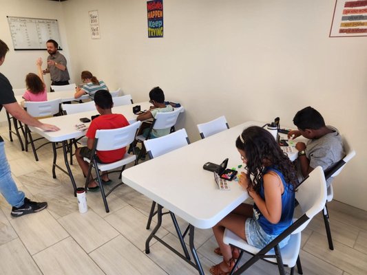 A series of Day Camp & Class photos! - In our Day Camps, Classes, Events, & Tournaments -- Students use Strategy Games & Logic Puzzles in a wide variety of Brain Sports and Brain Exercises designed to teach all students to think further ahead by developing deeper and more complex plans, to better manage their time, to better understand and learn from their mistakes, to improve their ability to communicate, negotiate, and compromise with their peers, all while socializing and having fun!  Students are taught basics if they are a beginner, intermediate strategies and tactics if they've mastered the basics, and advanced strategies and tactics while also learning to process and calculate more and more possibilities. 
The VAST majority of students that attend a FREE TRIAL CLASS enjoy it and want to continue learning with us. Students genuinely enjoy our classes and look forward to returning week to week! Parents often say that BRAIN POWERS DAY is their child's favorite day of the week! 
Students also commonly state that our DAY CAMPS are their favorite! Students often signed up for 4 hours ask us to call their parents to see if they can stay longer. Students that stay they full day (up to 9 hours!) still often say "mom/dad, can you wait 5-10 more minutes so I can finish this last game?" when parents arrive to pick them up... 
Students learn to CARE about their effort at BRAIN POWERS!
We have many parents noticing their students efforts in regular school also improving, as we do not just teach the games and the skills that come with them, but we also motivate your kids to think ahead about their lives and futures, how their choices today will impact tomorrow, and how they can begin to plan ahead and take their academics a bit more diligently as early as Kindergarten!!! -- by providing them with high energy instructors, who teach and inspire with life lessons, real world & kid appropriate examples, and who help cultivate environments where the students look forward to making friendships and learning together. 
In fact, many students between 9-15 often state that they are hopeful that they will develop enough skills at BRAIN POWERS and maintain effort in their normal schooling as well so that when they're 16 and older, they can begin to work at BRAIN POWERS.
Currently; 2 former students have progressed far enough with what we focus on, that they are now both 17 and driving themselves to our classes, tournaments, and camps, to attend and participate as a student/competitor, or sometimes to attend as a student assistant! They are both developing skills now as students but also as future instructors! 
If you're interested and would like to learn more, give us a call (or text!) at 623-321-4123
You may also visit our website at: www.k12brainpowers.com