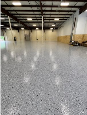 Commercial Warehouse Floor Transformation - This massive commercial warehouse project showcases the ultimate transformation from a dusty, worn-out raw concrete foundation to a high-performance, showroom-ready facility. Our expert team at Atlas Epoxy Floors stepped in to handle the extensive concrete preparation and install a seamless, heavy-duty commercial flake floor coating engineered to withstand the most demanding industrial environments.

The Challenge: Worn, Dusty, and Uneven Concrete
As seen in the before picture, the original concrete slab was heavily worn, stained, and deeply contaminated. The space was littered with construction debris, uneven patches, and a failing, chalky surface that generated endless concrete dust, a major hazard for equipment, electronics, and worker health. A space this size required a professional-grade solution that would eliminate dust, repair surface imperfections, and provide a perfectly uniform base capable of enduring heavy machinery.

Our Process: Precision Prep & Flawless Execution
True durability starts with meticulous preparation. We began by thoroughly clearing the space and utilizing heavy-duty industrial diamond grinders to open up the concrete pores, remove surface contaminants, and level out imperfections. Once the slab was flawlessly prepped and patched, we applied our multi-layered commercial epoxy system, broadcasting a dense blend of high-durability gray, black, and white flakes. We finished the project with a high-performance polyaspartic topcoat to seal the system.

The Result: Industrial Strength Meets Modern Style
The after picture highlights a stunning, mirror-like finish that completely redefines the warehouse. The ultra-glossy surface dramatically amplifies the overhead lighting, creating a bright, safe, and highly productive work environment.

This premium flake floor system delivers incredible long-term benefits for the business:
> Industrial-Grade Durability: Formulated to easily withstand heavy forklift traffic, pallet jack rollers, tool drops, and intense daily wear.
> Chemical & Stain Resistance: Protects the underlying concrete against harsh automotive fluids, oil spills, and chemical stains.
> Dust Elimination & Easy Maintenance: Eliminates concrete dusting entirely, turning a high-maintenance nightmare into a seamless, sweep-and-mop surface.
> Enhanced Workplace Safety: The dense flake broadcast creates an integrated, slip-resistant texture that helps prevent workplace slips and falls.

From a gritty, dark warehouse to a pristine, professional hub, Atlas Epoxy Floors delivers unmatched commercial flooring solutions across Connecticut.
