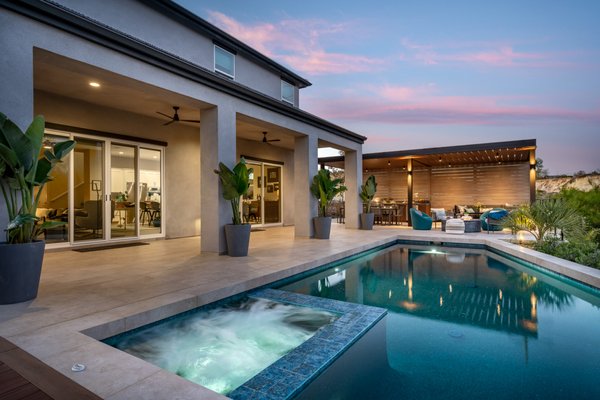 Contemporary Carlsbad Pool & Spa - Our clients wanted a minimalist contemporary design that would complement their home’s architecture and would include a backyard retreat complete with a swimming pool and all of the amenities and have it screen the power lines and deflect the traffic and noise of the busy street below them. A welcoming mahogany horizontal hardwood gate invites guests into the backyard side entrance. The area opens into a modern design of large gray and tan porcelain pavers in an offset pattern with black beach rocks. A custom aluminum patio-covered structure practically covers the power lines and aesthetically provides a sleek modern structure to house a full outdoor kitchen complete with stainless steel barbecue and side burner, refrigerator, storage drawers, and long countertops on either side of the barbecue, perfect for serving and preparation. The stainless steel chord railings provide an elegant contemporary backdrop to the living room area and the unusual poured black cement circular firepit added to the contemporary style of this backyard. The pool, with its unique geometrical lines, creatively hangs over the existing bank giving the pool a “floating” feeling. A sauna sits in front of an existing oak tree and is highlighted by LED lighting making for a gorgeous backdrop to the evening sunset. Contemporary Carlsbad Pool & Spa - Our clients wanted a minimalist contemporary design that would complement their home’s architecture and would include a backyard retreat complete with a swimming pool and all of the amenities and have it screen the power lines and deflect the traffic and noise of the busy street below them. A welcoming mahogany horizontal hardwood gate invites guests into the backyard side entrance. The area opens into a modern design of large gray and tan porcelain pavers in an offset pattern with black beach rocks. A custom aluminum patio-covered structure practically covers the power lines and aesthetically provides a sleek modern structure to house a full outdoor kitchen complete with stainless steel barbecue and side burner, refrigerator, storage drawers, and long countertops on either side of the barbecue, perfect for serving and preparation. The stainless steel chord railings provide an elegant contemporary backdrop to the living room area and the unusual poured black cement circular firepit added to the contemporary style of this backyard. The pool, with its unique geometrical lines, creatively hangs over the existing bank giving the pool a “floating” feeling. A sauna sits in front of an existing oak tree and is highlighted by LED lighting making for a gorgeous backdrop to the evening sunset.