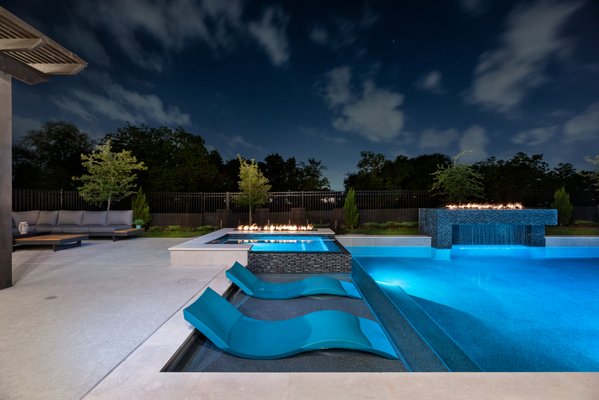 Modern Backyard Elegance - Escape to your own private sanctuary - a backyard paradise designed for modern tranquility. Immerse yourself in the sleek lines of a contemporary spa, its smooth surface reflecting the warm glow of the adjacent linear fire pit. Stretch out on sun-kissed blue ledge loungers, their vibrant hue juxtaposing perfectly with the geometric pools paved in cool stone. Let the gentle sound of a cascading rain curtain soothe your senses, while flames dance across the fire wall perched atop this gorgeous water feature. Every detail whispers of luxury, from the intricate tilework adorning the custom grotto to the cascading spa spillway. Modern Backyard Elegance - Escape to your own private sanctuary - a backyard paradise designed for modern tranquility. Immerse yourself in the sleek lines of a contemporary spa, its smooth surface reflecting the warm glow of the adjacent linear fire pit. Stretch out on sun-kissed blue ledge loungers, their vibrant hue juxtaposing perfectly with the geometric pools paved in cool stone. Let the gentle sound of a cascading rain curtain soothe your senses, while flames dance across the fire wall perched atop this gorgeous water feature. Every detail whispers of luxury, from the intricate tilework adorning the custom grotto to the cascading spa spillway.