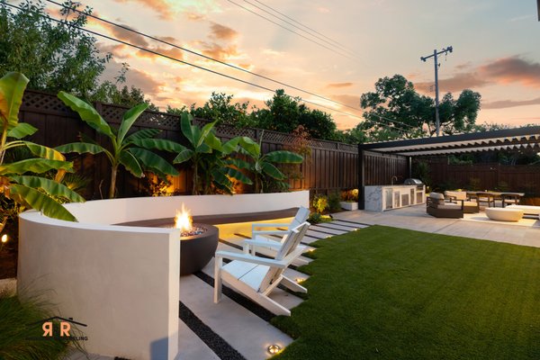 The Canna Project | Backyard Remodel - The Canna Project in San Jose, CA is a fully custom backyard transformation built by R&R Backyard Remodeling, creating a modern outdoor environment for entertaining, relaxing, and everyday living.

The project features a custom aluminum louvered pergola covering a complete outdoor living and dining area, along with a custom outdoor kitchen finished with porcelain surfaces and built in stainless steel appliances. A custom curved bench wraps around the fire pit area, creating an intimate gathering space surrounded by lush landscaping.

Porcelain paving, artificial turf, custom concrete stepping pads, decorative rock, integrated drainage, raised planters, and carefully placed landscape lighting connect the different areas throughout the backyard. Every detail was custom built to maximize the space and create a warm, modern atmosphere that feels just as inviting at night as it does during the day.

Built from start to finish by R&R Backyard Remodeling.