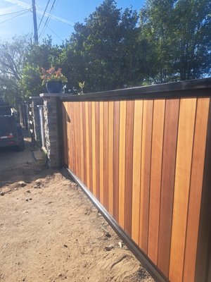 Driveway Entry Gate - This project involved the replacment of the original, bent, rusty wrought iron gate.
We started by removing the gate itself as well as a section of block wall to create a 22 ft. wide opening. We then anchored 4 inch 80 wall square tubing into 3x3x4 ft. footers to support the weight of such a wide driveway gate. 
We custom fabricated a 2in square tube frame, then stained and installed some very nice old growth straight grain cedar and installed an automatic opener to complete this beautiful new driveway entry gate, completely transforming the look of this property.