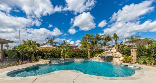 Riverside Refreshing Freeform - This custom freeform pool offers a truly relaxing retreat with a natural rock waterfall and hidden grotto, creating a resort-style experience right in your backyard. It features elegant flagstone coping, a spacious Baja shelf perfect for lounging, and a stacked stone raised spa with a soothing spillover into the pool.

The outdoor living area is equally impressive, complete with a freestanding patio cover and a fully equipped kitchen that includes a grill, smoker, and built-in pizza oven—ideal for entertaining. In the evenings, unwind by the cozy firepit area or enjoy the unique, calming ambiance of the custom-built artificial watering tree, designed to mimic the tranquil sound of rain.

Whether you're hosting or relaxing, this backyard was built to impress.