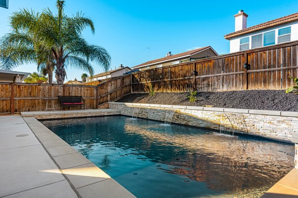 Pool Build in Menifee - This pool was built into a slope using precise engineering and execution. Stone veneer wall. Water features, and concrete caps. We also did all of the concrete, outdoor kitchen, Patio Cover and artificial grass.