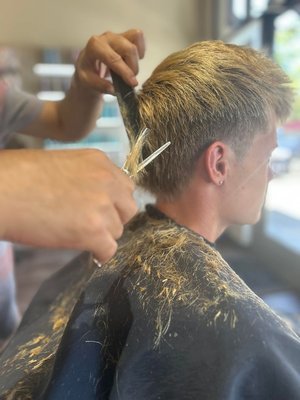Men's Cut - A professional men's haircut typically begins with a consultation to discuss the client's desired look. The hair is then shampooed and conditioned to cleanse and prepare it for cutting. The stylist proceeds with the haircut, shaping the hair to the client’s specifications using scissors, clippers, or both.  The hair is then blow-dried and styled with products to achieve the desired look. Finally, the stylist may offer hair care advice and styling tips to help the client maintain the style at home. The result is a tailored haircut that suits the client's individual needs.