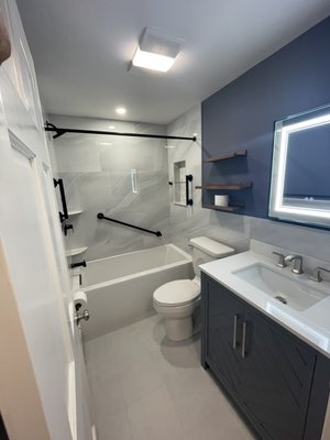 Bathroom Remodeling - This full bathroom remodel combines sleek design with everyday functionality. Large-format marble-look tiles, a deep soaking tub, and a bold navy vanity create a clean, contemporary look.

We added matte black grab bars and hardware for both style and safety, floating wood shelves for extra storage, and a backlit mirror to brighten the space. A perfect balance of comfort, elegance, and practicality.