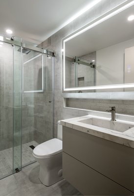 Ultra Modern Bathroom - From white chunky subway tile and pedestal sink to this ultra modern and sleek design. This bathroom was transformed to a clean and modern retreat with a focus on functionality. Large format porcelain tile, frameless glass shower enclosure, and a floating integrated sink creates a seamless feel. An illuminated mirror adds both light and luxury, enhancing the simplicity of the design while keeping the space bright. Ultra Modern Bathroom - From white chunky subway tile and pedestal sink to this ultra modern and sleek design. This bathroom was transformed to a clean and modern retreat with a focus on functionality. Large format porcelain tile, frameless glass shower enclosure, and a floating integrated sink creates a seamless feel. An illuminated mirror adds both light and luxury, enhancing the simplicity of the design while keeping the space bright.