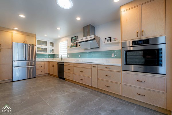 Rosemead Coastal-Inspired Kitchen Remodel - Rona Home Remodeling transformed this Rosemead home with a stunning kitchen remodel. We created an L-shaped layout to enhance flow, installing light birch cabinetry with matte gold handles, white quartz countertops with subtle gray veining, and an aqua glass subway tile backsplash for a fresh coastal vibe. Stainless steel appliances, including a French door refrigerator, induction cooktop, and wall oven, ensure efficiency, while floating white shelves add personalized warmth. Gray porcelain tile flooring with marble-like veining and recessed lighting create a bright, airy space, perfect for family gatherings. Rosemead Coastal-Inspired Kitchen Remodel - Rona Home Remodeling transformed this Rosemead home with a stunning kitchen remodel. We created an L-shaped layout to enhance flow, installing light birch cabinetry with matte gold handles, white quartz countertops with subtle gray veining, and an aqua glass subway tile backsplash for a fresh coastal vibe. Stainless steel appliances, including a French door refrigerator, induction cooktop, and wall oven, ensure efficiency, while floating white shelves add personalized warmth. Gray porcelain tile flooring with marble-like veining and recessed lighting create a bright, airy space, perfect for family gatherings.