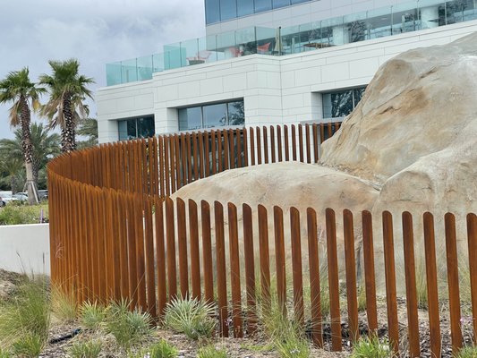 Brown and Brown Cheetah Fence - The Brown and Brown building in Daytona Beach features a life-like cheetah sculpture on the property. To help keep the sculpture and rock protected they needed a custom fence solutions that wouldn't detract from the beauty of the piece. We built 220 corten steel posts at varying heights to give the finished fence a sloped effect. Corten steel was used for its aged, rusted look. Brown and Brown Cheetah Fence - The Brown and Brown building in Daytona Beach features a life-like cheetah sculpture on the property. To help keep the sculpture and rock protected they needed a custom fence solutions that wouldn't detract from the beauty of the piece. We built 220 corten steel posts at varying heights to give the finished fence a sloped effect. Corten steel was used for its aged, rusted look.