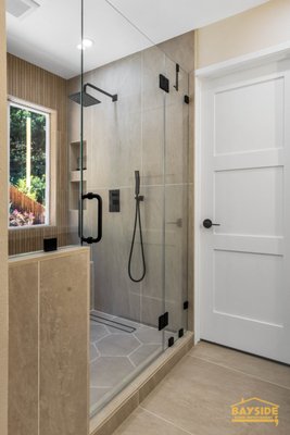 6th PL Residence - Bathroom remodel - Modern bathroom with a sleek glass shower, freestanding tub, and dual-sink vanity. Features wood accents, hexagon tiles, and a large window with a scenic view. By Bayside Home Improvement. 6th PL Residence - Bathroom remodel - Modern bathroom with a sleek glass shower, freestanding tub, and dual-sink vanity. Features wood accents, hexagon tiles, and a large window with a scenic view. By Bayside Home Improvement.