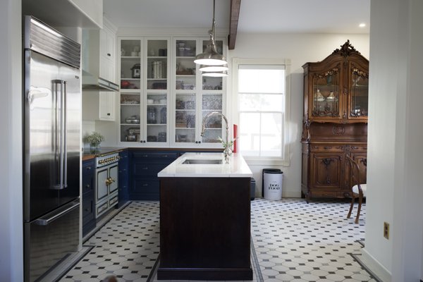 Traditional with European Flair Kitchen Remodel - This kitchen remodel artfully bridges timeless design with contemporary functionality, creating a space that is as enduring as it is practical. A thoughtfully curated palette of materials, finishes, and lighting transforms the kitchen into the warm, inviting heart of the home.
Floor-to-ceiling white cabinetry wraps the perimeter, amplifying natural light from surrounding windows to create an open, airy atmosphere. Clean panel detailing keeps the aesthetic refined while maximizing storage capacity. Glass-front cabinet doors introduce depth and offer an elegant opportunity to display fine dishware and cherished kitchen essentials.
Rich navy lower cabinets provide a bold, grounding contrast that lends the space personality and dimension. Warm wood countertops introduce an organic quality, softening the interplay between crisp whites and cool tones with natural warmth.
At the center of it all, a generous island anchors the layout — featuring a dark wood base, a light contrasting countertop, integrated storage, and a farmhouse apron sink with a high-arc faucet. It serves seamlessly as both a culinary workspace and a casual gathering spot.
Vintage-inspired metal pendant lights hang above the island, providing focused task lighting with character. The cooking station makes a confident statement with a brass-detailed range, a custom range hood, and a classic subway tile backsplash as its backdrop.
Underfoot, traditional hexagonal floor tiles tie the design together, reinforcing the timeless aesthetic with subtle visual texture.
The result is a kitchen that is meticulously considered — blending classic charm with modern-day livability, perfectly suited for everything from everyday meals to memorable entertaining. Traditional with European Flair Kitchen Remodel - This kitchen remodel artfully bridges timeless design with contemporary functionality, creating a space that is as enduring as it is practical. A thoughtfully curated palette of materials, finishes, and lighting transforms the kitchen into the warm, inviting heart of the home.
Floor-to-ceiling white cabinetry wraps the perimeter, amplifying natural light from surrounding windows to create an open, airy atmosphere. Clean panel detailing keeps the aesthetic refined while maximizing storage capacity. Glass-front cabinet doors introduce depth and offer an elegant opportunity to display fine dishware and cherished kitchen essentials.
Rich navy lower cabinets provide a bold, grounding contrast that lends the space personality and dimension. Warm wood countertops introduce an organic quality, softening the interplay between crisp whites and cool tones with natural warmth.
At the center of it all, a generous island anchors the layout — featuring a dark wood base, a light contrasting countertop, integrated storage, and a farmhouse apron sink with a high-arc faucet. It serves seamlessly as both a culinary workspace and a casual gathering spot.
Vintage-inspired metal pendant lights hang above the island, providing focused task lighting with character. The cooking station makes a confident statement with a brass-detailed range, a custom range hood, and a classic subway tile backsplash as its backdrop.
Underfoot, traditional hexagonal floor tiles tie the design together, reinforcing the timeless aesthetic with subtle visual texture.
The result is a kitchen that is meticulously considered — blending classic charm with modern-day livability, perfectly suited for everything from everyday meals to memorable entertaining.