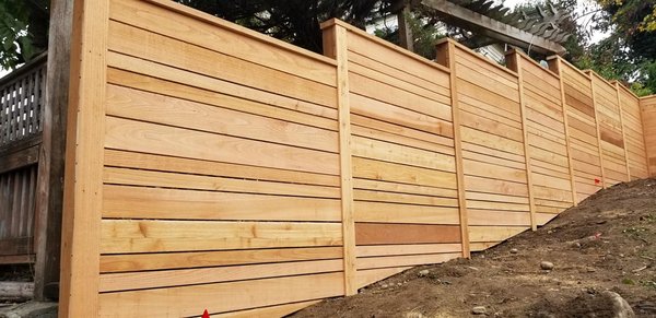 Horizontal style using rough cut fence boards with alternating board widths - Horizontal style using rough cut fence boards with alternating board widths and pressure treated retainment to contour uneven surface and hill Horizontal style using rough cut fence boards with alternating board widths - Horizontal style using rough cut fence boards with alternating board widths and pressure treated retainment to contour uneven surface and hill