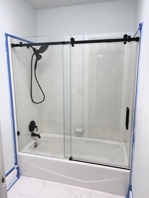 Before and After Bathtub Sliding Door. Holladay, Utah 2025 - This outdated, framed bathtub sliding door was replaced with a sleek, frameless glass enclosure. The new seamless design modernizes the look, making the bathroom feel more open and bright while showing off the tub. View photo 2 for before photo.