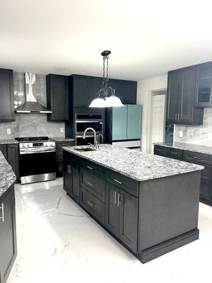 Kitchen Transformation - Check out this stunning remodel featuring brand-new cabinets, sleek countertops, modern backsplash, and elegant floor tiles. This kitchen remodel features dark wood shaker-style cabinetry, sleek granite countertops, a polished gray stone backsplash, and glossy white floor tiles with gold veining. The combination creates a modern, elegant, and functional space. Kitchen Transformation - Check out this stunning remodel featuring brand-new cabinets, sleek countertops, modern backsplash, and elegant floor tiles. This kitchen remodel features dark wood shaker-style cabinetry, sleek granite countertops, a polished gray stone backsplash, and glossy white floor tiles with gold veining. The combination creates a modern, elegant, and functional space.