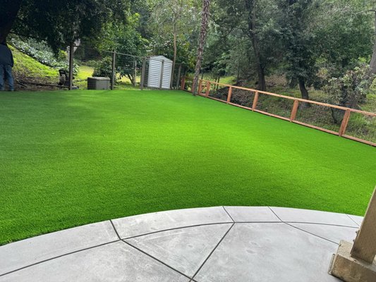 Concrete, fence and turf installation - We completely reimagined this outdoor space to blend durability with a modern aesthetic. The transformation features a clean, reinforced concrete patio with a professional broom finish and a sleek hog-wire fence crafted from premium redwood and pressure-treated wood to preserve the natural creek views.
To create a vibrant, low-maintenance landscape, we replaced old mulch with lush synthetic turf, professionally leveled with a crushed rock and decomposed granite base. For the finishing touch, we removed outdated lattice and installed a metal roof drainage system under the existing deck, turning a wasted area into a dry, functional space. The result is a stunning, multi-purpose backyard built to last. Concrete, fence and turf installation - We completely reimagined this outdoor space to blend durability with a modern aesthetic. The transformation features a clean, reinforced concrete patio with a professional broom finish and a sleek hog-wire fence crafted from premium redwood and pressure-treated wood to preserve the natural creek views.
To create a vibrant, low-maintenance landscape, we replaced old mulch with lush synthetic turf, professionally leveled with a crushed rock and decomposed granite base. For the finishing touch, we removed outdated lattice and installed a metal roof drainage system under the existing deck, turning a wasted area into a dry, functional space. The result is a stunning, multi-purpose backyard built to last.