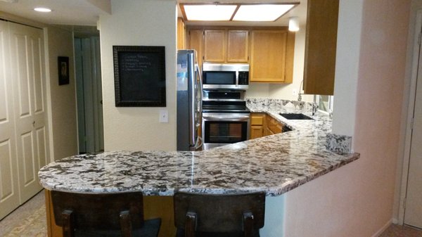Kitchen Counter Upgrade - The condo was built in the 80's and wasn't a high end finishes offering. The appeal was location. We removed tired ceramic tile with wood edging and cut out a wall blocking the kitchen space and living space from each other. We install a new sub top, South American granite counters and a new single basin composite sink with an industrial style faucet.